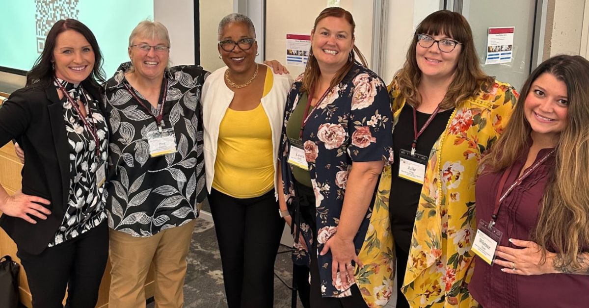 A group of six women stand together smiling.