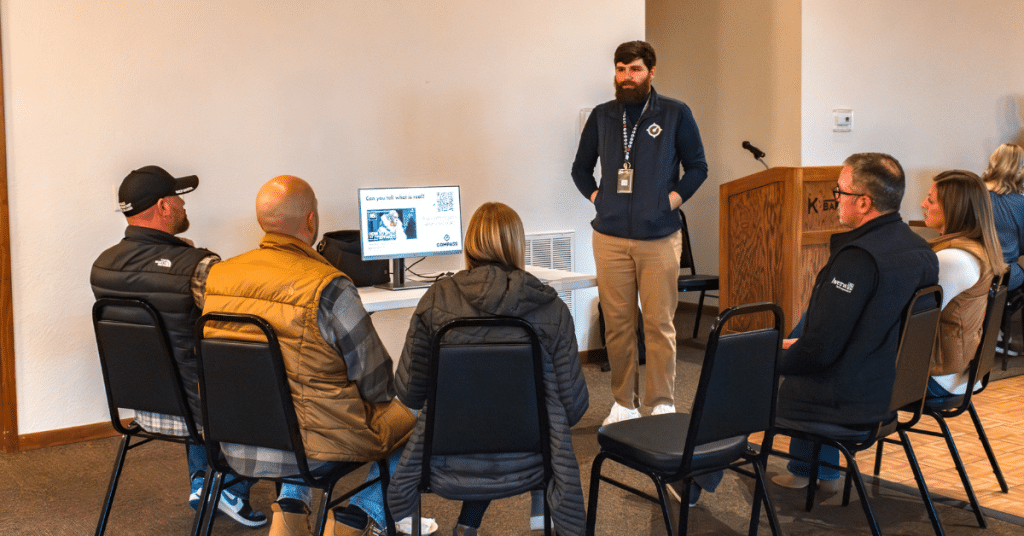 Man standing in front of a computer presenting to a seated group of five people.